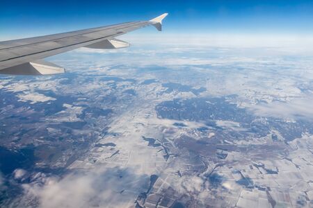 A plane silver wing during a flight over white clouds and a winter land is on the photoの写真素材