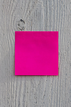 A square pink or red note paper with copy space is hanging on a gray wooden fence. Horizontal...