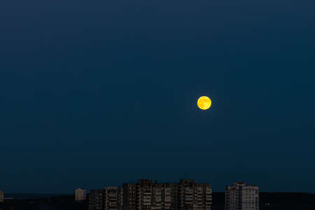 The yellow round Moon and gray silhouettes of buildings are is on the navy blue sky background at nightの写真素材