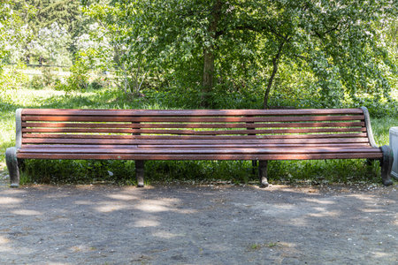 Old wooden painted brown color beautiful bench with black wrought-iron legs stands by the walkway in...