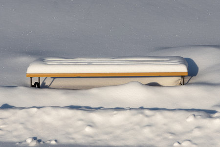 Wooden painted brown color beautiful bench stands with white snow in a park in winterの写真素材
