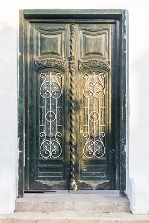 A green old door with metal bars is outside a white house on a sunny day. Verticalの写真素材