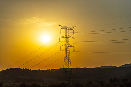Silhouette of a black electricity transmission tower with power lines stretching across the sky at...