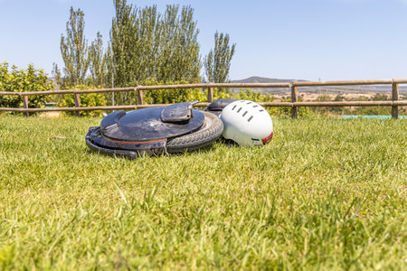 Electric unicycle with a helmet lie on the green lawn against a wooden fenceの写真素材