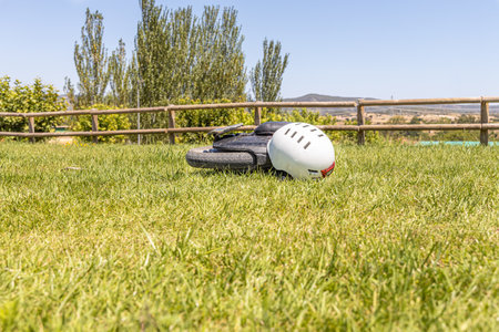 Electric unicycle with a helmet lie on the green lawn against a wooden fenceの写真素材
