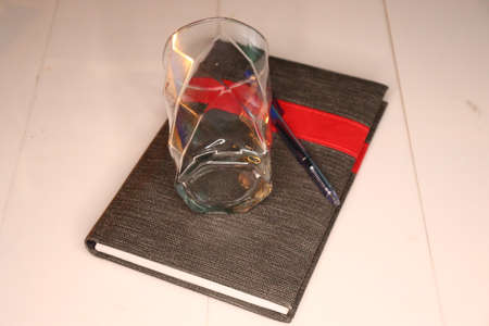 A glass with a red ribbon and a notebook on a white backgroundの写真素材