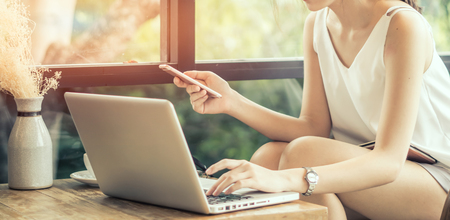 Woman right hand touching on laptop computer mouse pad while using smartphone in coffee shop. Freelance worker on workday concept.の写真素材