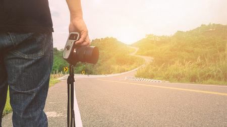 Man holding a camera standing on the street in mountain road  .A traveler or photographer taking pictures on the road trip.の写真素材