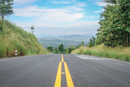 Country road Flanked by vegetation, mountain backgroundの写真素材