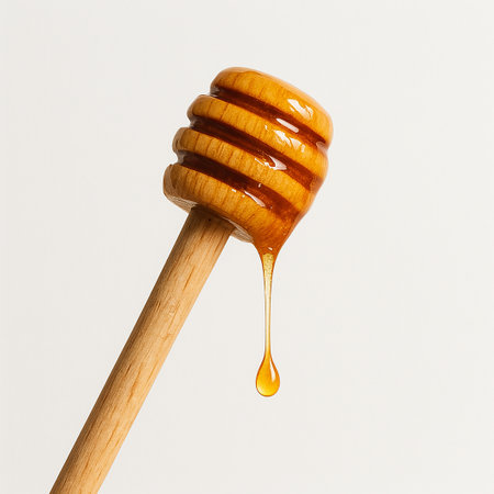 Honey dripping from a wooden honey dipper isolated on white backgroundの素材
