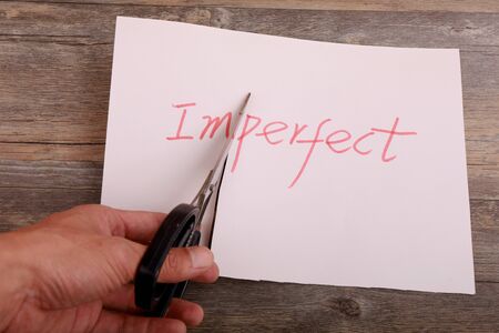 A scissor cuts perfect from imperfect on the desk.の写真素材