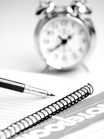 Pen, books and alarm clock on table