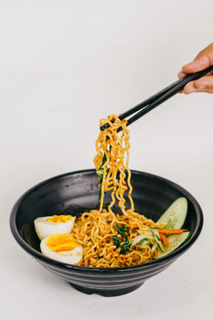 Noodles with vegetables and egg in black bowl on white background