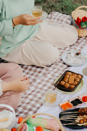 cropped shot of woman holding cup of tea while having picnic in park