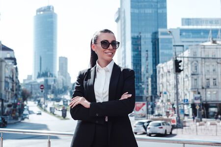 Confident at her business. Beautiful young businesswoman in sunglasses looking away with smile while standing outdoors.の写真素材