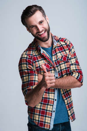 You are awesome! Handsome young man looking at camera with smile and gesturing thumb up while standing against white backgroundの写真素材