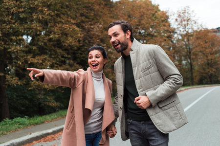 This way! Young beautiful couple bonding to each other while walking in the park in autumn