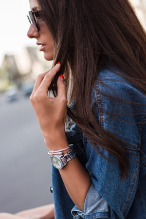 Cool and stylish. Close-up of beautiful young woman in jeans jacket looking away with smile while sitting outdoorsの写真素材