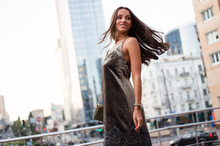 Sunset in her hair. Beautiful young woman in velvet dress looking away with smile while standing outdoors