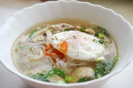 Bowl of vietnamese chicken pho with an poached egg. Pho ga with egg. Rice noodle soup.
