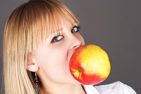 beautiful blond holding a big apple in the teethの写真素材
