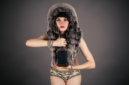 beautiful woman in a fur hat with a bottle of whiskeyの写真素材