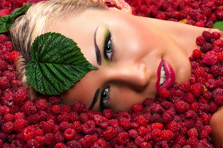beautiful woman face in raspberries with leavesの写真素材