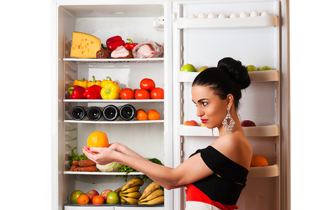 luxurious rich woman with orange in hands and fridgeの写真素材