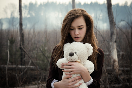 Young girl hugs a teddy bear on the background of burnt forestの写真素材