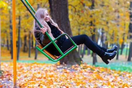 charming blond girl on swing in autumn parkの写真素材