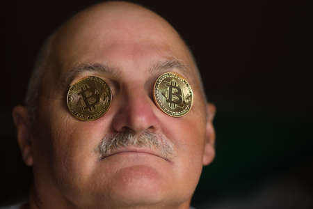 old man with bitcoin coins in eyesの写真素材