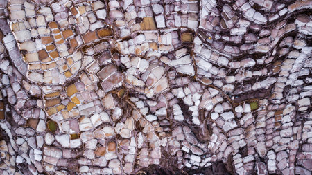 Aerial view of salt evaporation ponds at salt mine in Maras, Peru. Different shapes and colors of...
