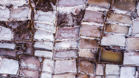 Aerial view of salt evaporation ponds at salt mine in Maras, Peru. Different shapes and colors of...