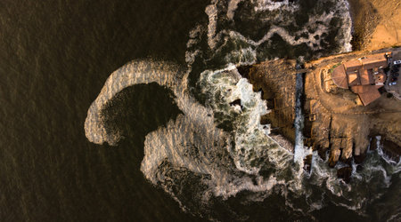 Aerial view on huge rock separated from the coast with waves crushing during the golden hour. Rocky...