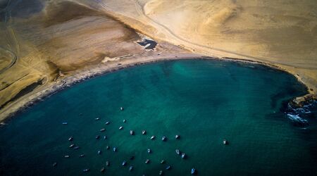 Aerial view of many fishing boats next to peninsula at the rocky coast of Peru. Little fishing boats from above. Dark green waters, rocky island, rocky, sandy coast.の写真素材