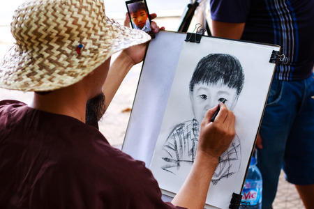 Vietnam Ho Chi Minh city May 28 2015: Street artist drawing with a pencil at the sample using smartphone Looked at a park in the cityのeditorial素材