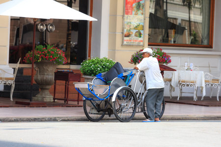 Hochiminh City, Vietnam - September 20, 2015: an old cyclo rider was standing front of a luxury...