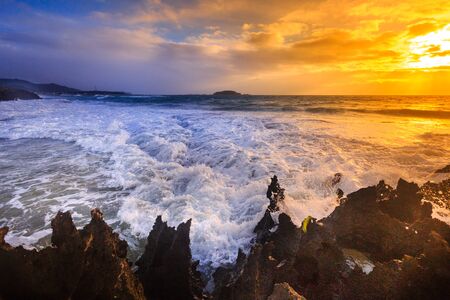 Blurry waves over rocky beach at dawn with the beautiful sunriseの写真素材