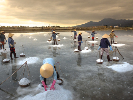 Ninh Thuan Province, Vietnam - February 28, 2016 :the women are working on salt field at dawn. Salt field Hon Khoi in Nha Trang, Viet Nam. Workers transporting salt from the fields Hon Khoi, Viet Nam.のeditorial素材