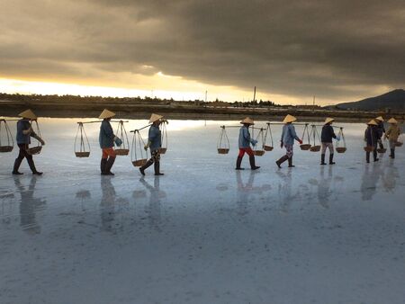 Ninh Thuan Province, Vietnam - February 28, 2016 :the women are working on salt field at dawn. Salt field Hon Khoi in Nha Trang, Viet Nam. Workers transporting salt from the fields Hon Khoi, Viet Nam.のeditorial素材