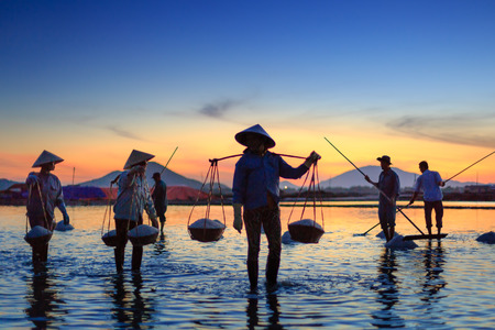 Khanh Hoa Province, Vietnam - July 30, 2016 :the women and men are working on salt field at dawn. Salt field Hon Khoi in Nha Trang, Viet Nam. Workers transporting salt from the fields Hon Khoi, Viet Nam.のeditorial素材