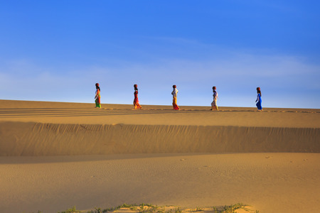 Phan Rang town, Ninh Thuan province, Vietnam - November 26, 2016 : Cham women in traditional dress walking across sand dunes to collecting water near Phan Rang, Vietnam. Many Cham people retain their traditional ways.のeditorial素材