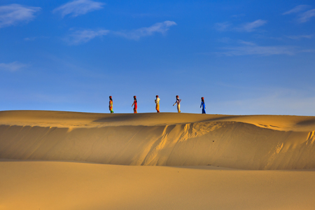 Phan Rang town, Ninh Thuan province, Vietnam - November 26, 2016 : Cham women in traditional dress walking across sand dunes to collecting water near Phan Rang, Vietnam. Many Cham people retain their traditional ways.のeditorial素材