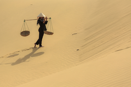 Ninh Thuan province, Viet Nam - December 24, 2016: A peasant girl carries a bamboo frame on the shoulder across sand dunes in Ninh Thuan province, Viet Namのeditorial素材