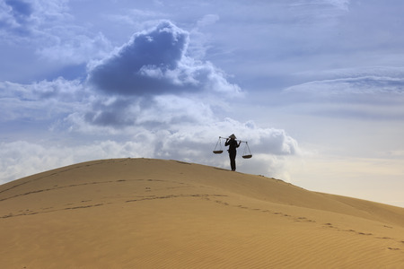Ninh Thuan province, Viet Nam - December 24, 2016: A peasant girl carries a bamboo frame on the shoulder across sand dunes in Ninh Thuan province, Viet Namのeditorial素材