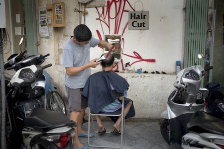 Hanoi capital, Vietnam - July 16, 2018: A barber cutting hair for his customers on the street in Hanoi's Old Quarter, Vietnamのeditorial素材