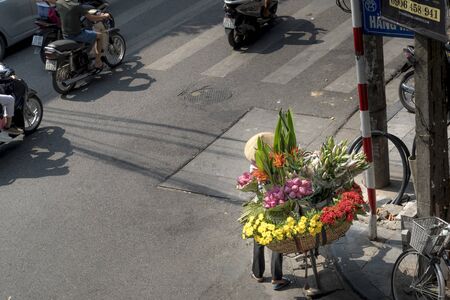 Hanoi capital, Vietnam - July 12, 2018: The street vendors in Hanoi, Vietnam. The Rural woman selling fresh flowers in a busy street.のeditorial素材