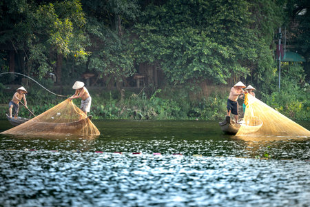 Hue city, Viet Nam - May 08, 2020: Vietnamese fishermen catching fish and throwing out two large yellow fishnet on a boat from the peaceful Nhu Y river in Hue, Vietnamのeditorial素材