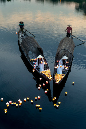 Hue City, Vietnam - May 8, 2020: Two Vietnamese girls with wihte tradition Ao Dai are lighting candle in lantern to pray in the river. Ao dai is famous traditional costume for the women in Vietnam.のeditorial素材