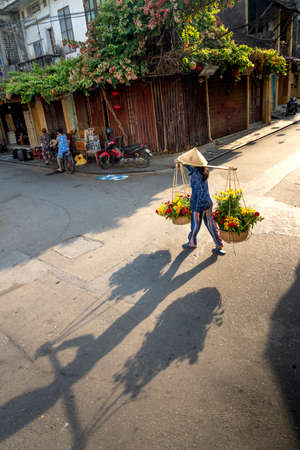 Hoi An Ancient Town, Quang Nam Province, Vietnam - May 10, 2020: Photo of a woman selling flowers on a pair of bamboo frames in Hoi An Ancient Town, Quang Nam Province, Vietnamのeditorial素材